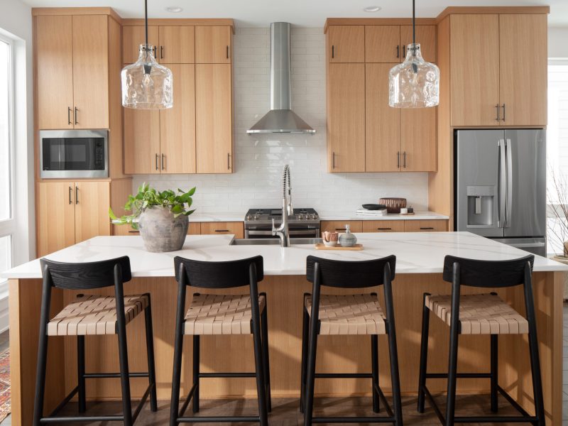 A kitchen from a back view of 4 black and cane counter stools overlooking a kitchen island with natural wood cabinets in the background.